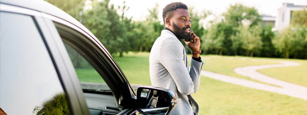 Businessman in a suit speaking on smartphone while standing outdoors near his luxury black car. Find Amarillo Texas car insurance.