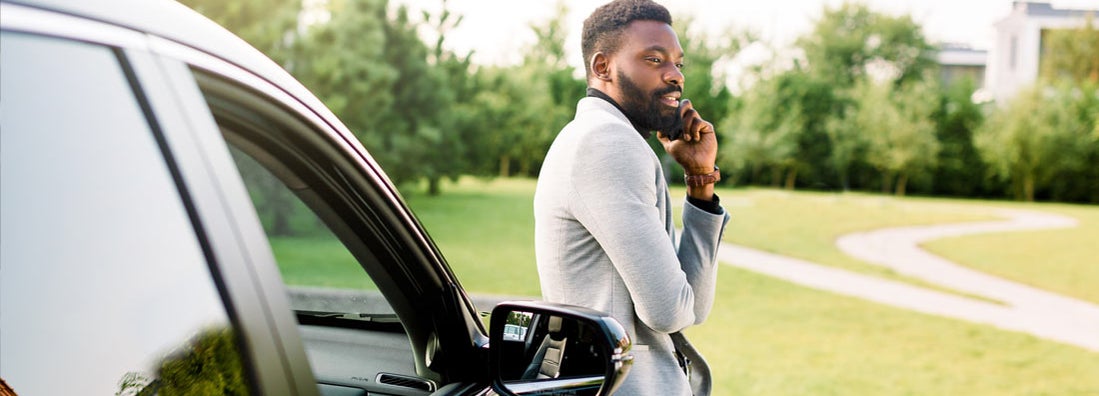 Businessman in a suit speaking on smartphone while standing outdoors near his luxury black car. Find Amarillo Texas car insurance.