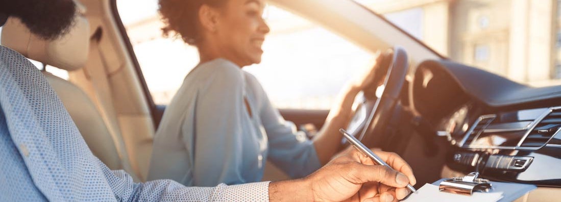 Young woman driving car, feeling inexperienced, instructor controlling and checking