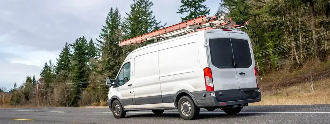 Cargo van with ladders on the roof driving. Find Alaska Commercial Vehicle Insurance.