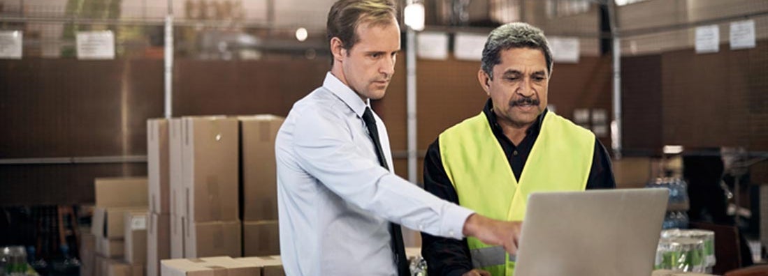 Warehouse worker discussing something on a laptop with his boss in a factory. Workers' Compensation and Employers Liability Exclusion.