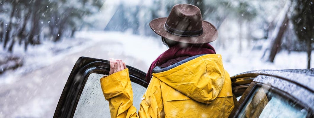 Female traveler with yellow rain coat driving on snowy day. Find Anchorage Alaska car insurance.