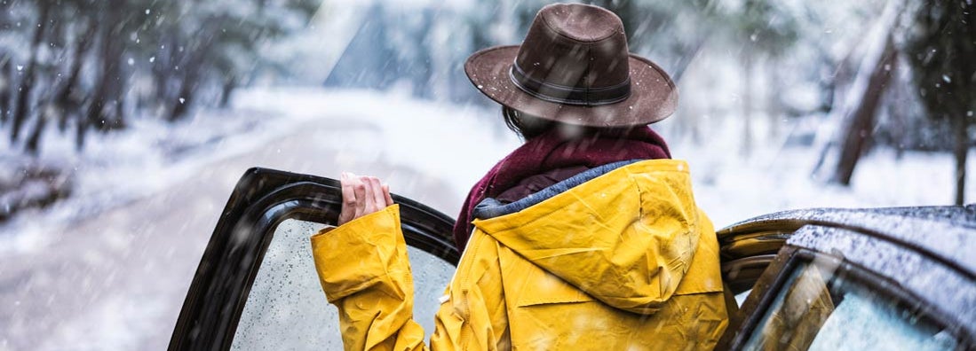 Female traveler with yellow rain coat driving on snowy day. Find Anchorage Alaska car insurance.