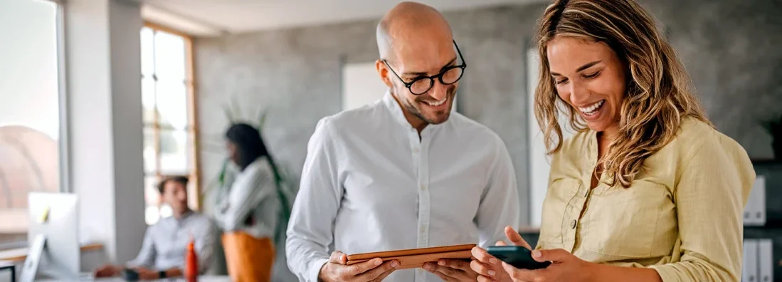 Businesswoman standing with colleague looking at phone in modern office. Business Insurance in Lake Oswego, Oregon.