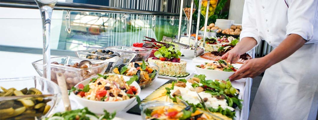Caterer serving a large buffet table full of delicious food.
