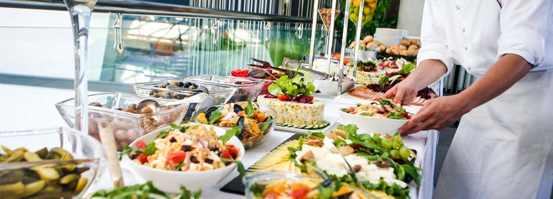 Caterer serving a large buffet table full of delicious food.