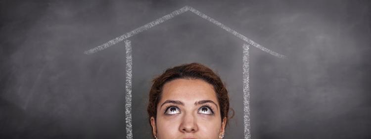 A woman looks up at a drawing of a house on a chalkboard, wondering.