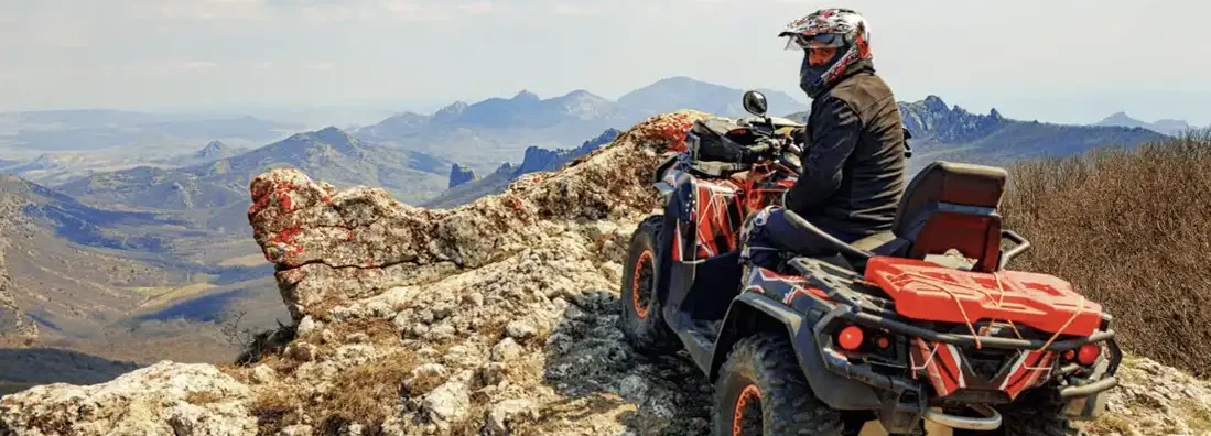 Man in helmet sitting on ATV quad bike in mountains. How Much Does ATV Insurance Cost?