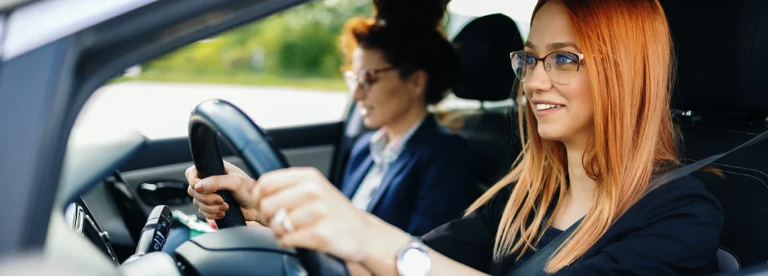 Woman learning how to drive car with her instructor. Find your learners permit insurance.