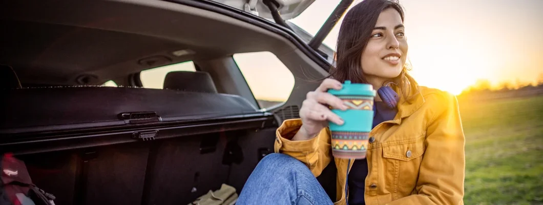 Woman resting in a car trunk with coffee during her road trip. Shelburne, Vermont Car Insurance.
