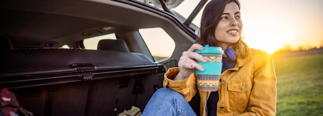 Woman resting in a car trunk with coffee during her road trip. Shelburne, Vermont Car Insurance.