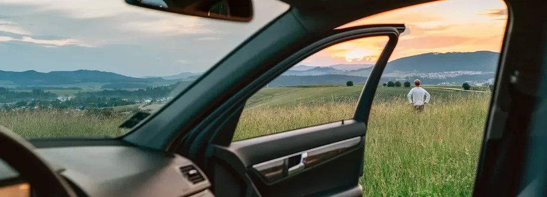Man standing in high grass and enjoying the sunset sky colors through the open car door view. How to Find the Best Car Insurance in Williston, North Dakota. 