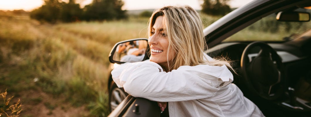 Young smiling woman sitting in car on dirt road in nature. Find Charleston South Carolina car insurance.