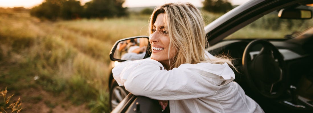 Young smiling woman sitting in car on dirt road in nature. Find Charleston South Carolina car insurance.