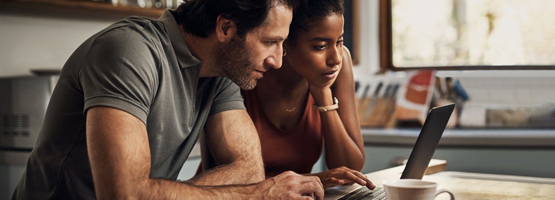 Couple using a laptop while doing their budget paperwork in their kitchen at home. 10 things to know about renewing insurance. 