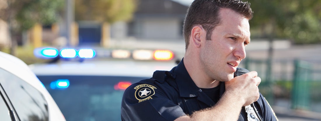 Police officer reaching for radio. Police car in background.