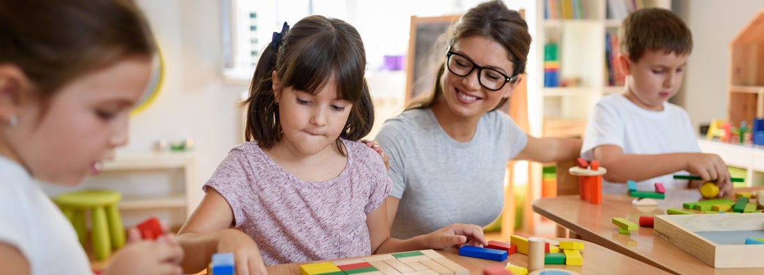 Preschool teacher with children playing with colorful wooden blocks