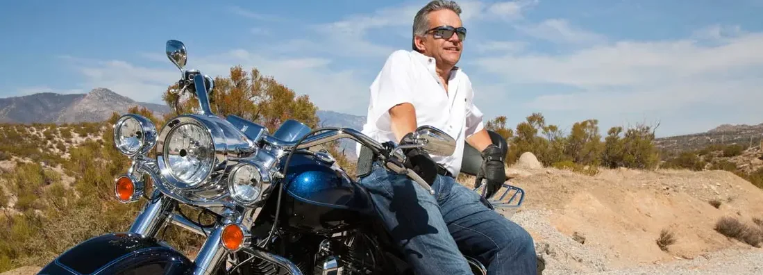 Senior man wearing sunglasses on motorcycle in desert. Find Arizona motorcycle insurance.