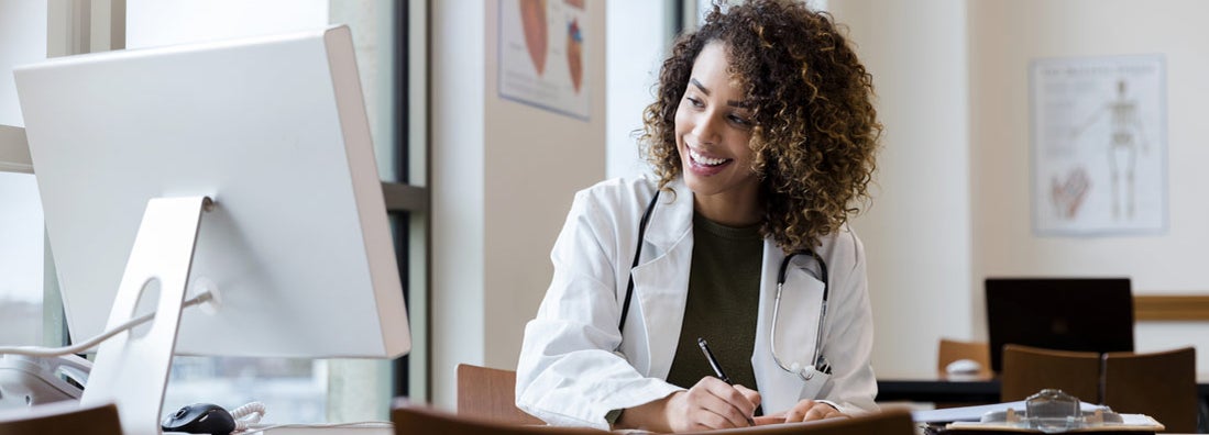 Doctor reviews her patient's records on her computer in her office. Find doctors liability insurance.