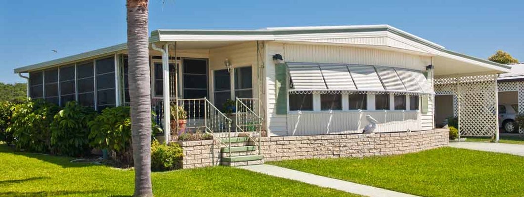 Mobile home with green lawn and palm tree, located in a tropical climate. Find HO7 mobile home insurance.