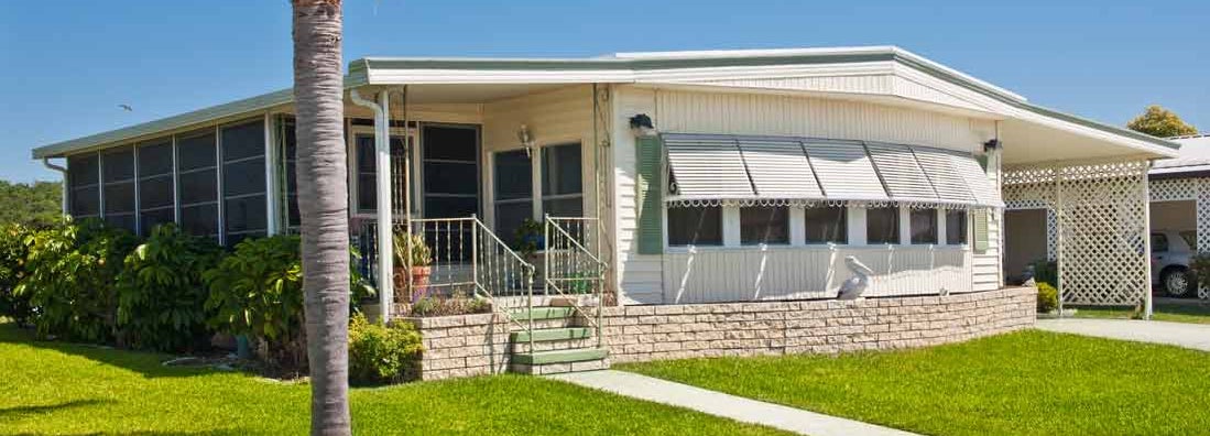 Mobile home with green lawn and palm tree, located in a tropical climate. Find HO7 mobile home insurance.