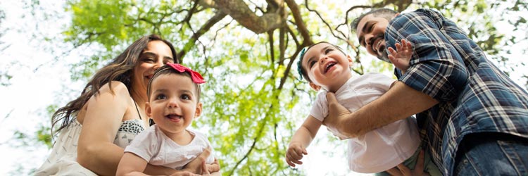 Low angle view of playful latin parents holding their twin girls and laughing in a horizontal medium shot outdoors.