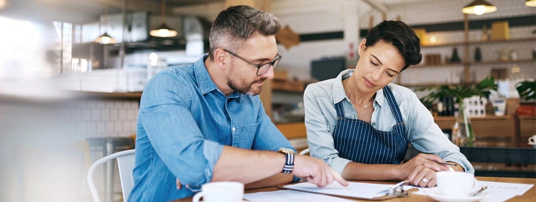 Business owners going through insurance paperwork together in their coffee shop. Find Business Insurance Discounts.