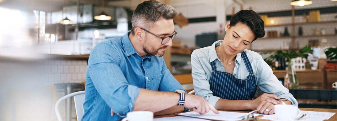 Business owners going through insurance paperwork together in their coffee shop. Find Business Insurance Discounts.