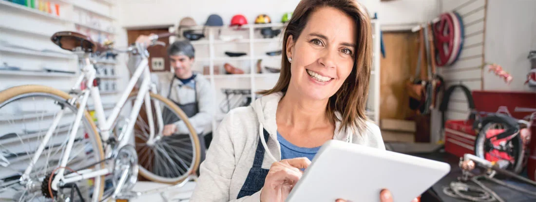 Married couple at their bicycle shop and woman looking at camera smiling holding a tablet. Do LLC Members Need Workers' Comp?