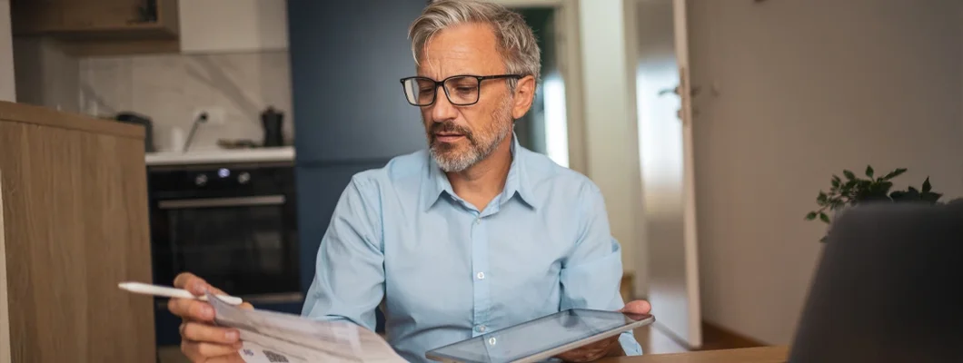 Man reviewing financial documents at home with tablet and laptop. How to Prevent Cybercrime.