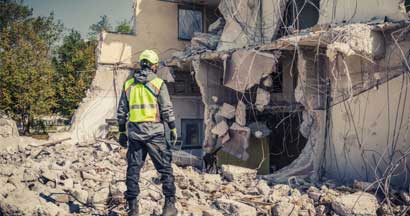 Rescuer search home ruins with help of rescue dog. Find Earthquake Safety Tips: How to Be Prepared in Case of Earthquakes.