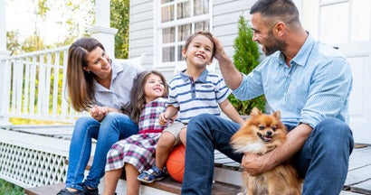 Happy family with two kids sitting in front of porch. Find Homeowners Liability Insurance.