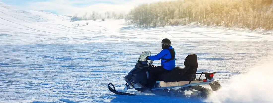 Man driving a snowmobile in Colorado. Snowmobile License Requirements & State Regulations.