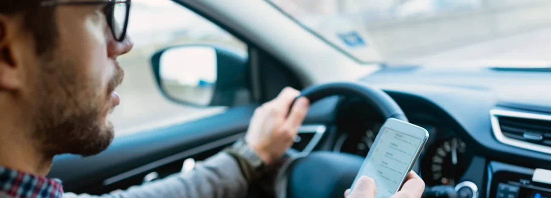 Close up of a businessman using mobile phone while driving. A State-by-State Guide to Distracted Driving Laws and Penalties.