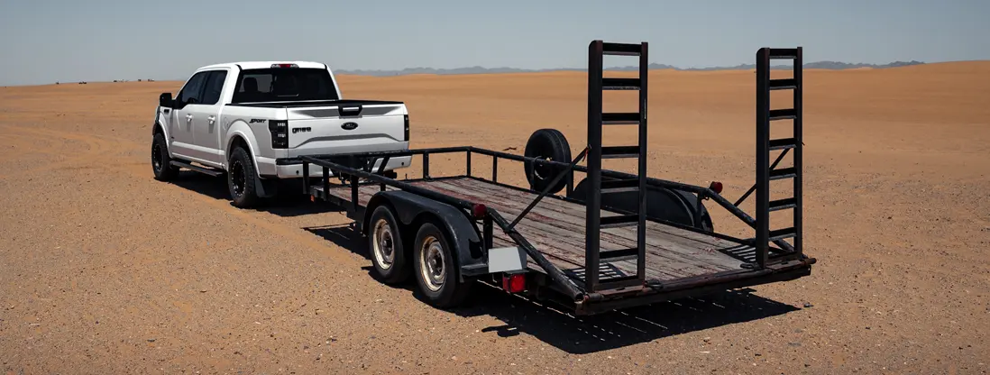 Flatbed utility trailer being towed by a white pickup truck. Find Flatbed Trailer Insurance.