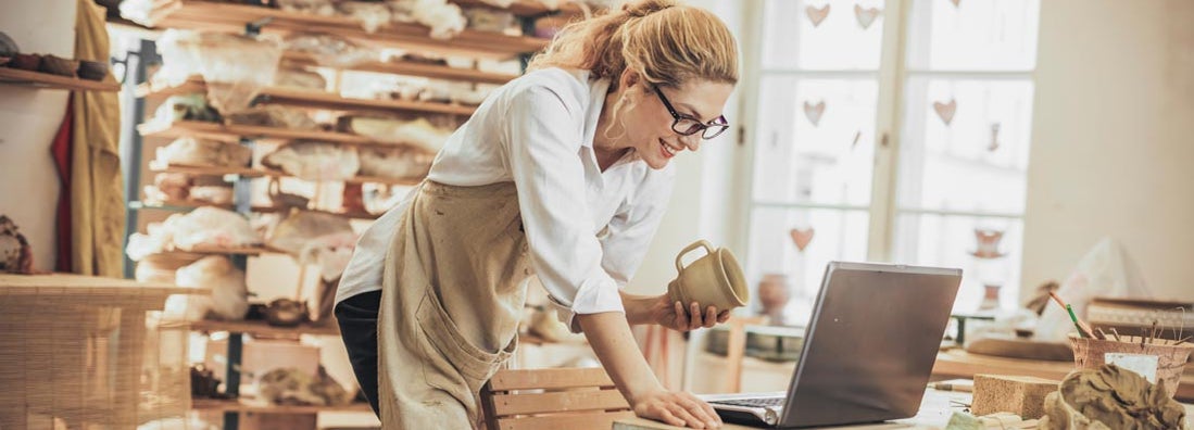 Potter entrepreneur using Shopify on laptop in workshop