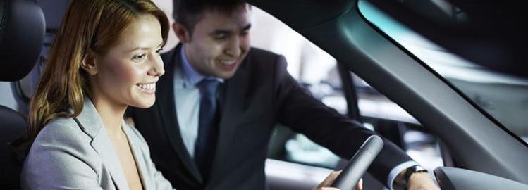 A woman sitting inside a car while her auto broker explains its features.