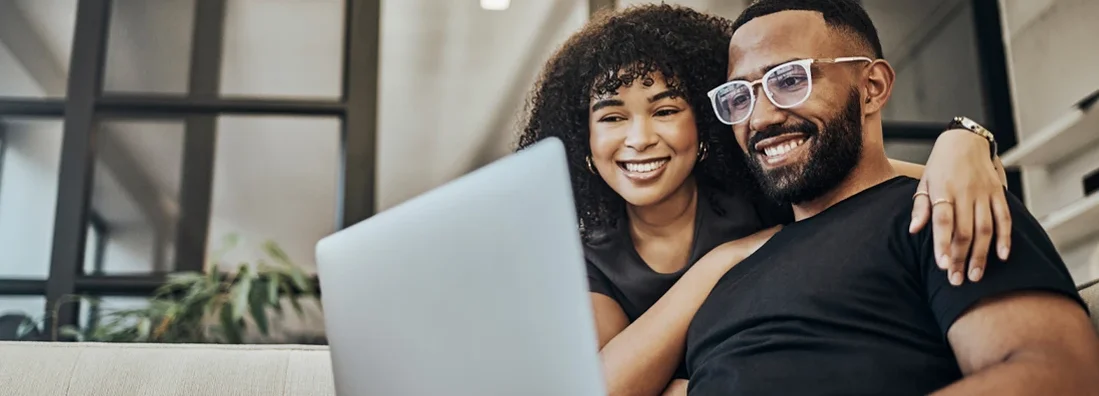 Couple on sofa researching insurance on laptop in living room. Find personal liability insurance for renters.