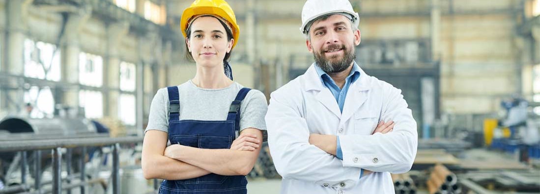 Two modern factory workers looking at camera while posing in industrial workshop. Find workers' compensation.