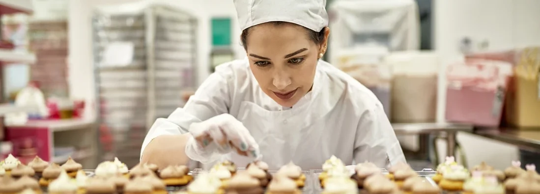 Focused baker decorating fresh batch of cupcakes in commercial kitchen. How to Find the Best Business Insurance in Clayton, Missouri.