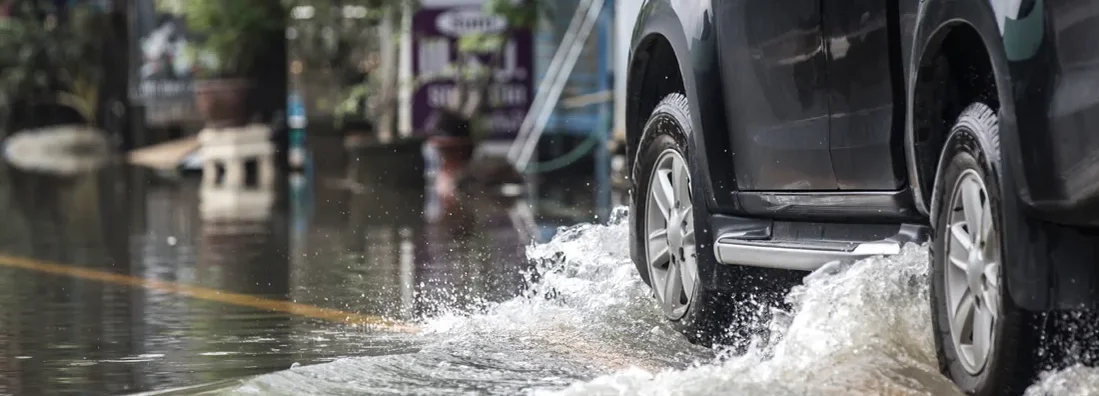 Black pickup truck driven through a flooded road. Does Car Insurance Cover Flood Damage?