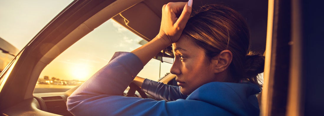 Sad woman having problems while driving a car at sunset. This is why your car insurance is making you broke.