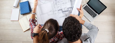 Young couple sitting on the floor and looking at the blueprint of new home.
