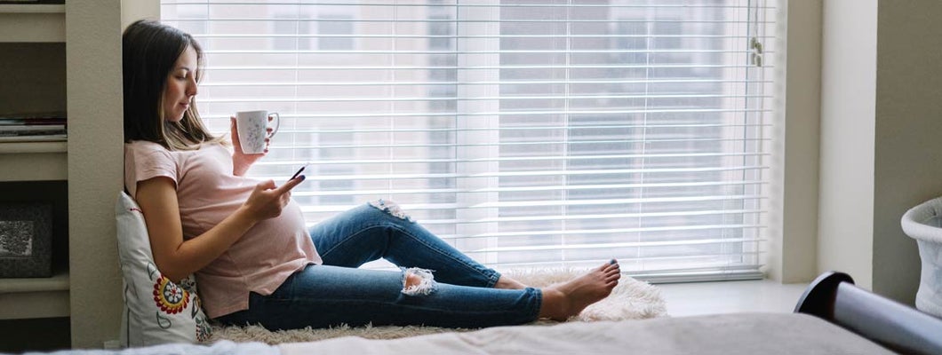 Pregnant woman using her smartphone at home. Find Health Insurance.