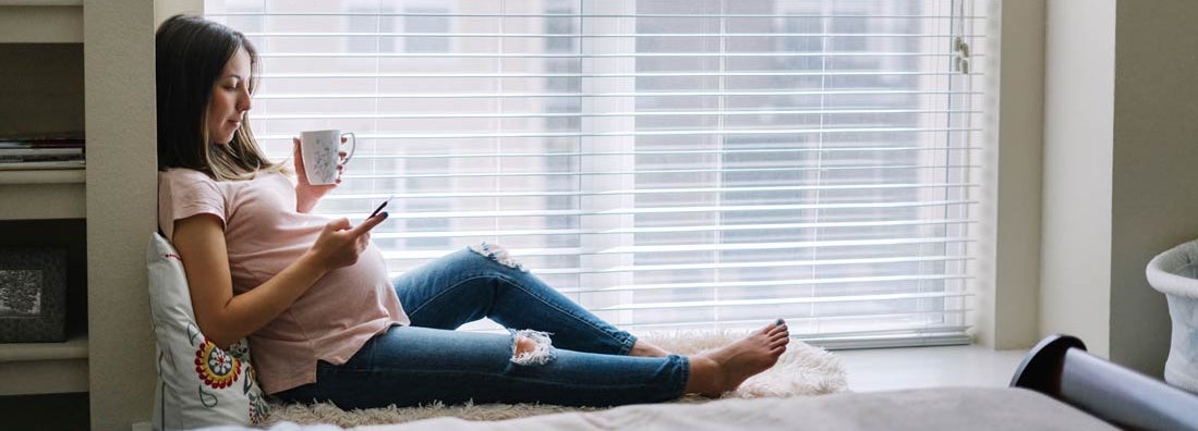 Pregnant woman using her smartphone at home. Find Health Insurance.