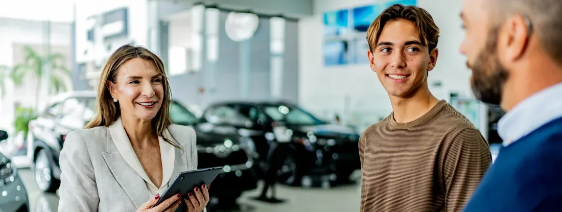 Father and son talking to saleswoman at car dealership. How to Pick out a Car for Your Teen Driver.