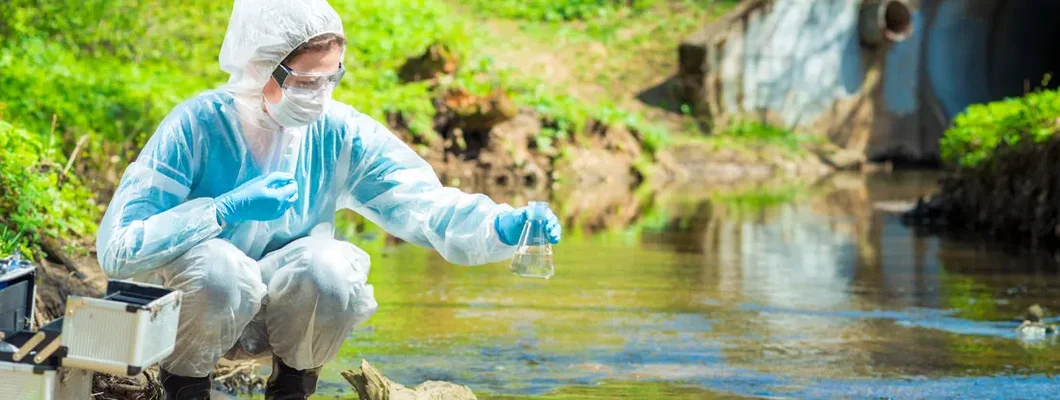 Environmental scientist with a flask takes a sample of water at the site of industrial discharge of water. Find Environmental & Pollution Liability Insurance.