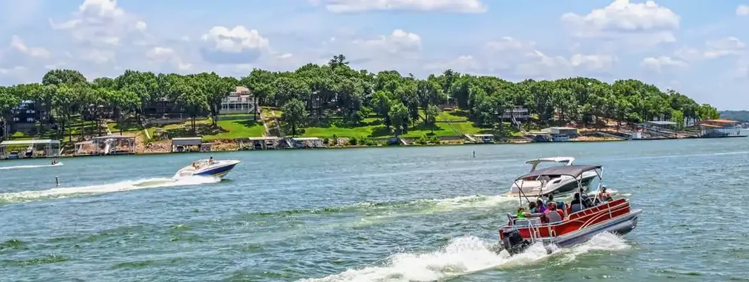 Pontoon boat and speedboat race down lake with luxury homes and docks on shore. Find Oklahoma Boat Insurance.