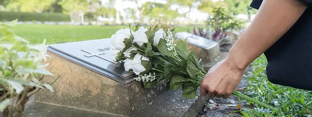 Woman laying white flowers on her family grave in beautiful green cemetery. Find funeral and burial insurance.