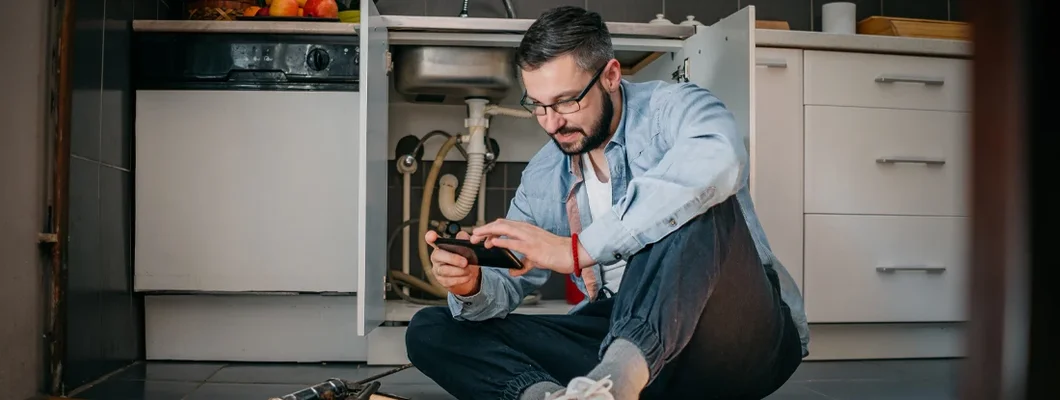 The plumber uses the phone. Find Home Repair Insurance.